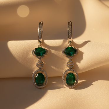 Front pair view of sterling silver green emerald double halo drop earrings on cream satin