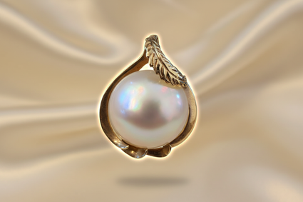 14K yellow gold mabe pearl feather bail pendant floating on cream satin backdrop with warm accent lighting