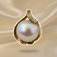 14K yellow gold mabe pearl feather bail pendant floating on cream satin backdrop with warm accent lighting