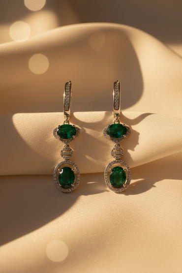 Front pair view of sterling silver green emerald double halo drop earrings on cream satin
