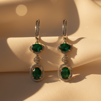 Front pair view of sterling silver green emerald double halo drop earrings on cream satin