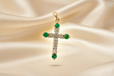 14K yellow gold emerald and diamond cross pendant floating on cream silk backdrop with warm accent lighting