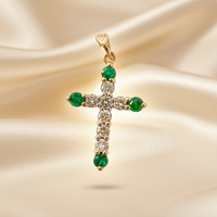 14K yellow gold emerald and diamond cross pendant floating on cream silk backdrop with warm accent lighting