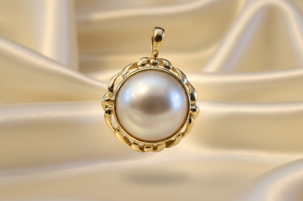 14K yellow gold mabe pearl enhancer pendant floating on cream satin backdrop with warm accent lighting