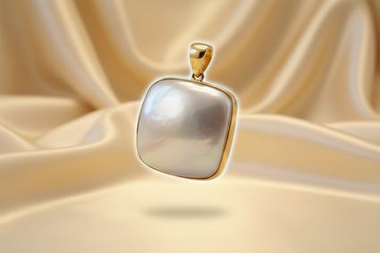 14K yellow gold cushion mabe pearl pendant floating on cream satin backdrop with warm accent lighting