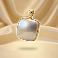 14K yellow gold cushion mabe pearl pendant floating on cream satin backdrop with warm accent lighting