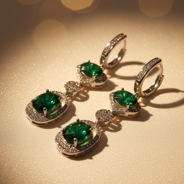 Side profile view of sterling silver green emerald and diamond halo drop earrings on cream satin